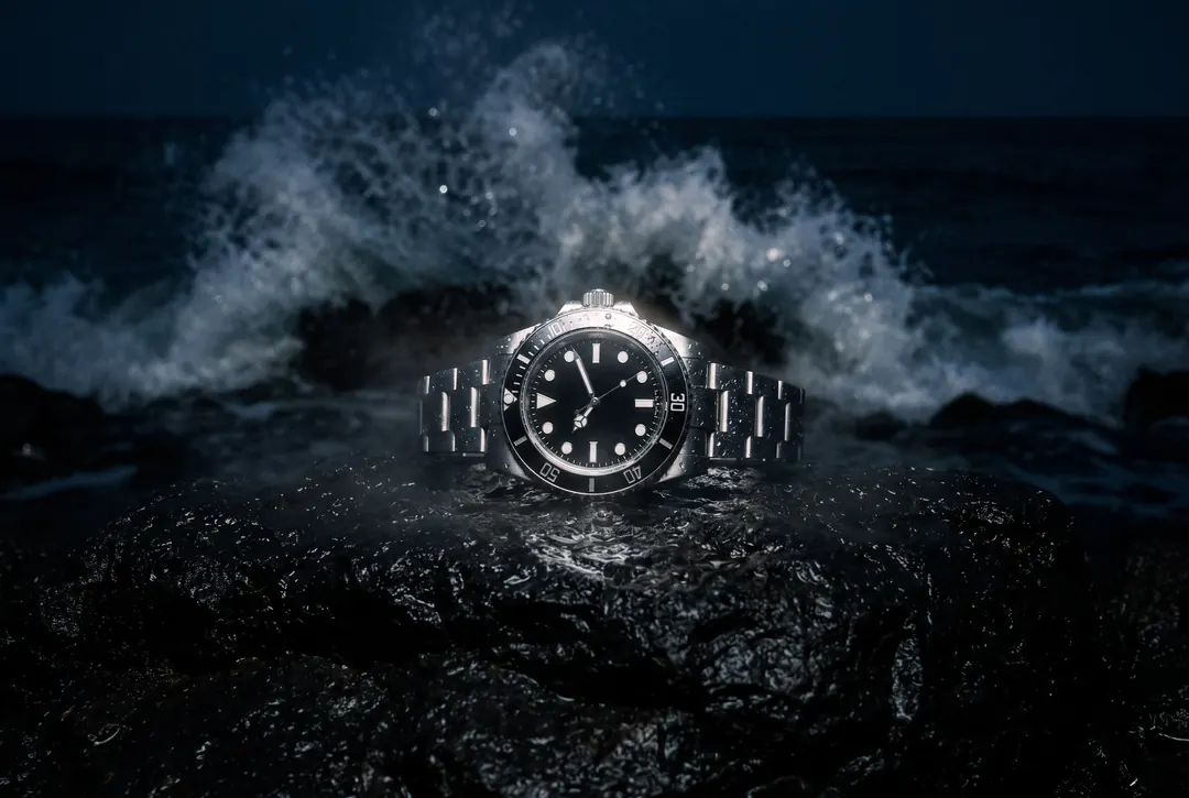 Wristwatch on wet black rock as a wave breaks behind