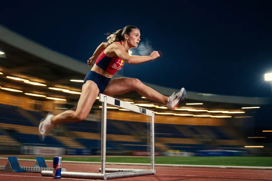 Hurdler clearing a hurdle under stadium floodlights