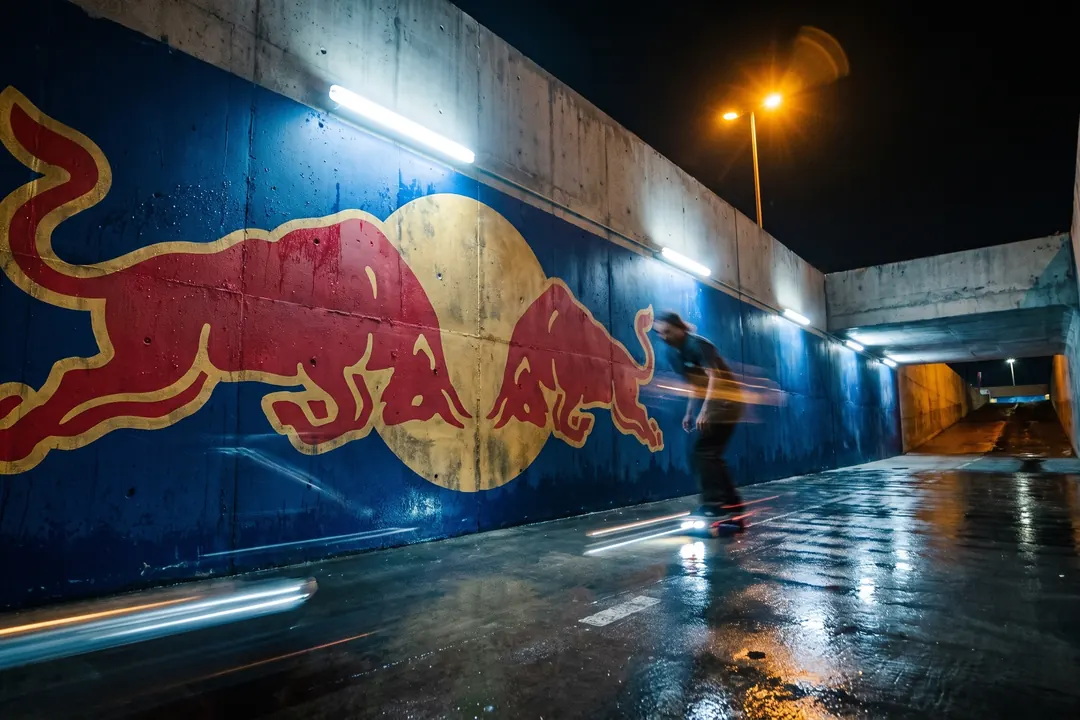 Skateboarder rolling past a painted mural in a night underpass