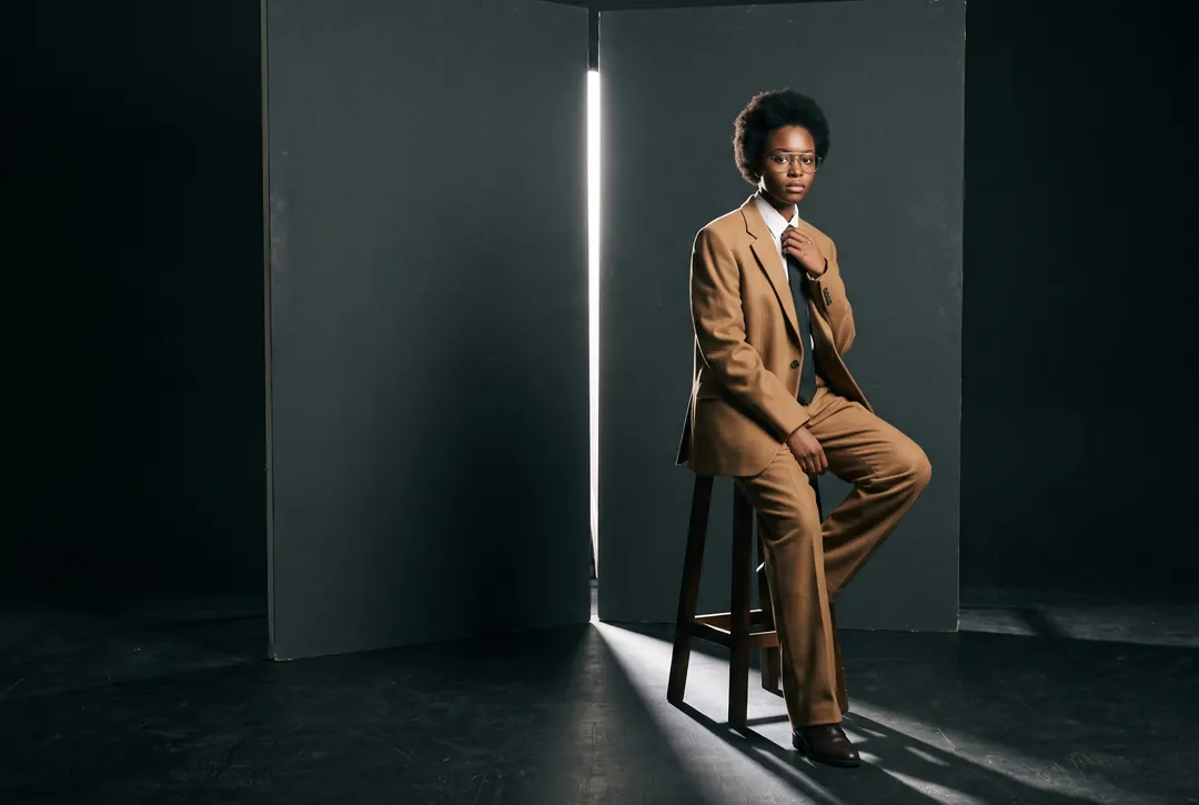 Model in a camel suit on a stool in a slit of hard light