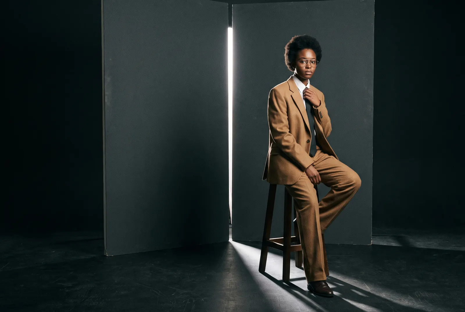 Model in a camel suit on a stool in a slit of hard light