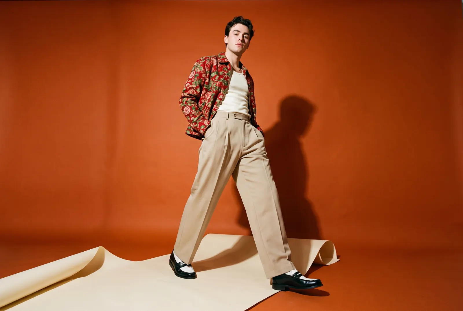 Menswear model striding on a cream path across an orange sweep