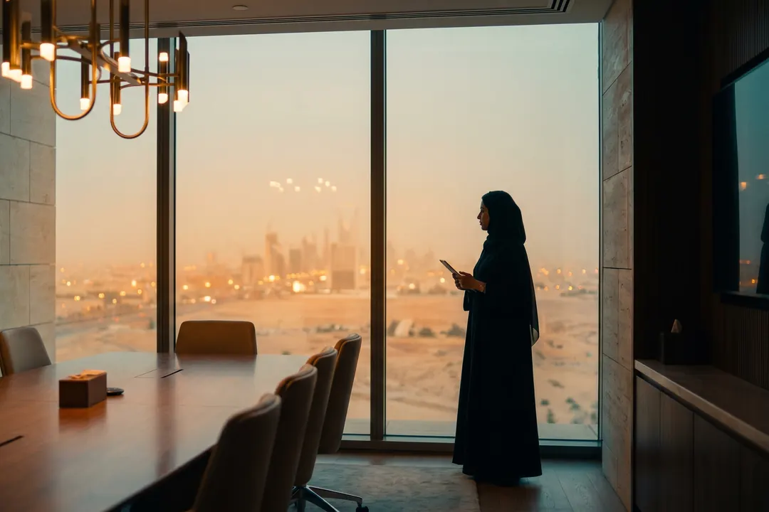 Woman in an abaya at a floor to ceiling window above the city