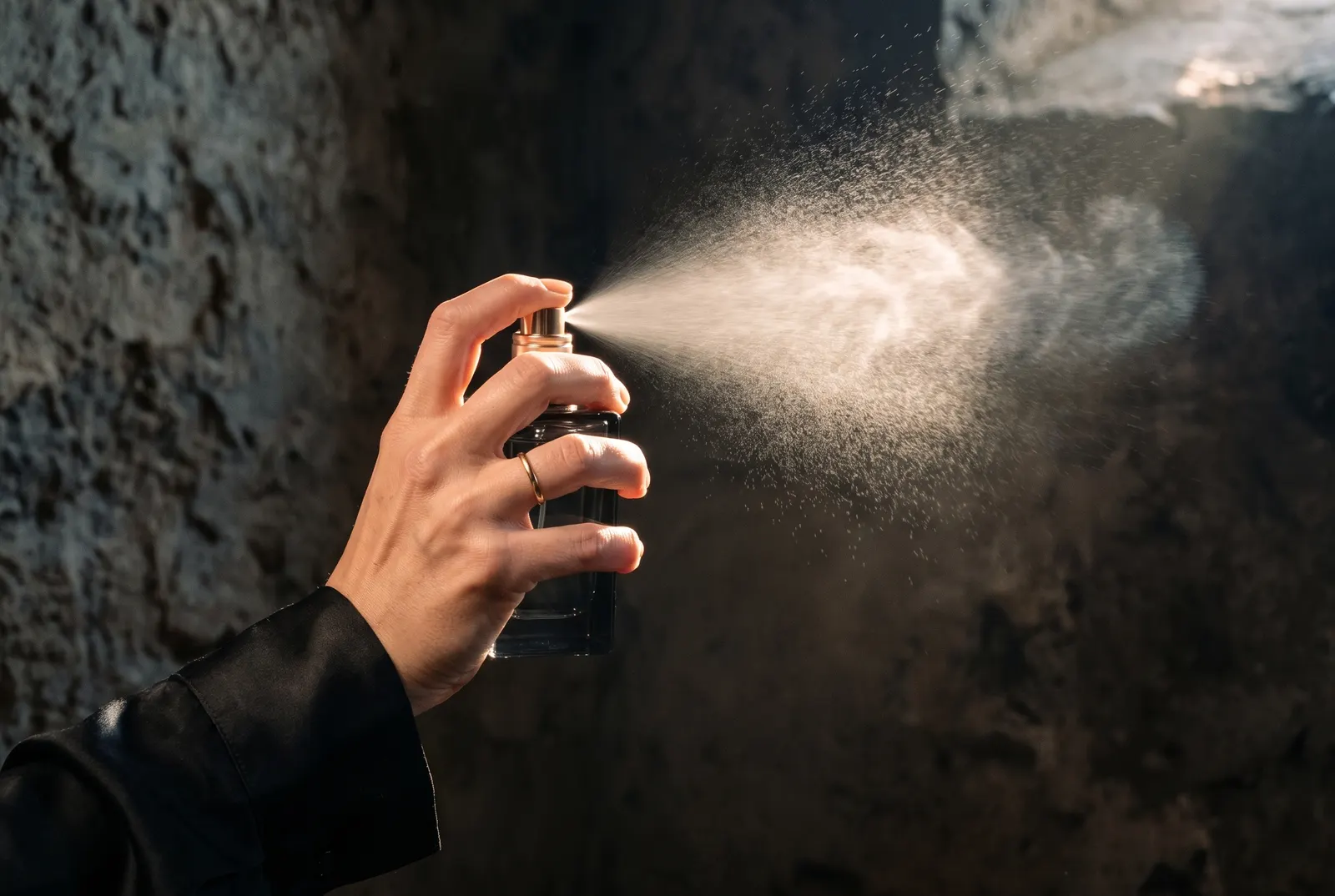 Hand spraying perfume into a beam of warm light